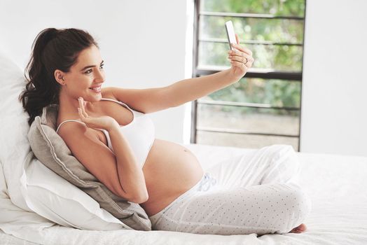 She wants to remember every moment of her pregnancy. a pregnant woman taking a selfie at home.