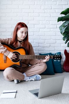 Young woman learning to play guitar at home