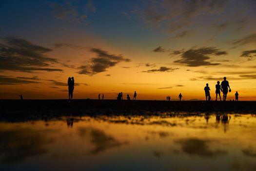 Silhouettes of people walking on the ocean floor after the evening tide. Incredible colors of the evening sky