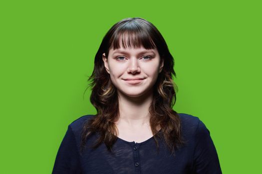 Headshot portrait of young female looking at camera on green background