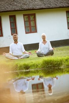 They found a tranquil spot to meditate together. Full length shot of a mature couple meditating beside a pond.