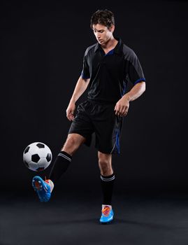 His technique is flawless. Full length studio shot of a handsome young soccer player isolated on black.