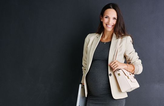 Maternity wear for the working woman. Studio portrait of a young pregnant businesswoman standing against a black background.