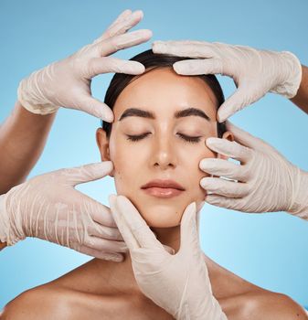 Plastic surgery, beauty and hands on the face of a woman isolated on a blue background in a studio. Feeling, skincare and doctors touching a model for a botox, cosmetics or dermatology consultation