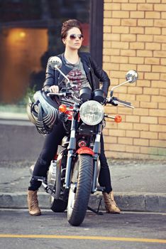 She makes that bike look good. a young and stylish female motorcycle rider outside.