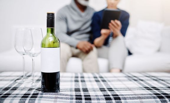 Everything goes well with a bottle of wine. an unrecognizable senior couple relaxing on a sofa with their bottle of wine and glasses waiting on a table at home.