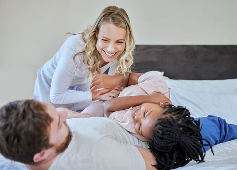 Foster parents tickle adoption kid in bedroom, family home and house for fun, bonding and quality time with love, care and happiness together. Happy black kid relax with mom, dad and diversity people