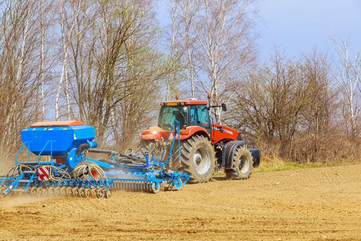 The tractor sows the field with grain in early spring. Modern technology works on a sunny day in the field.