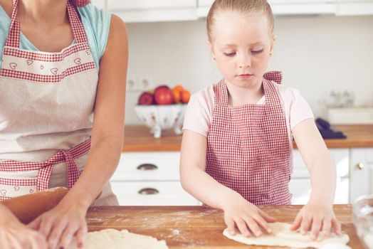 Focused on her task. Cute little girl baking in the kitchen with her mom.