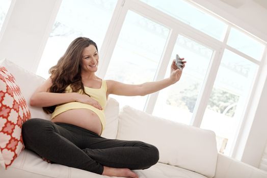 Selfie buddy on board. a young pregnant woman taking a selfie with her cellphone in her living.