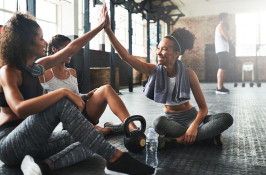 Behind every fit woman is another one cheering her on. young women giving each other a high five while taking a break at the gym.