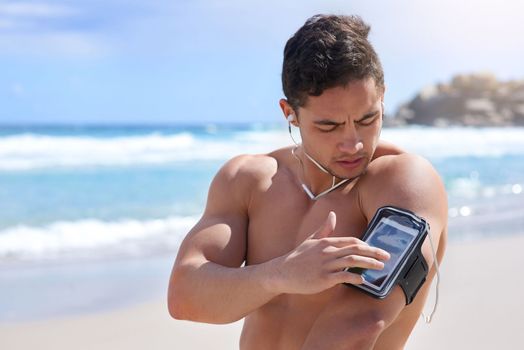 Getting his playlist ready. a handsome young man setting up his workout playlist on the beach.