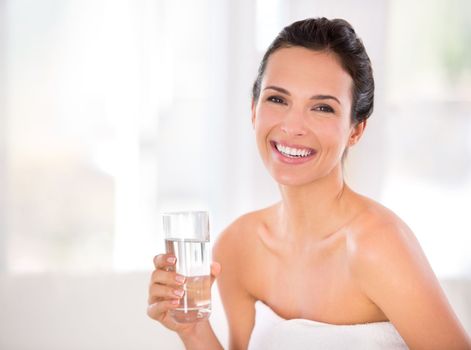 Water - a vital part of my skincare regime. Portrait of a beautiful woman holding a glass of water.