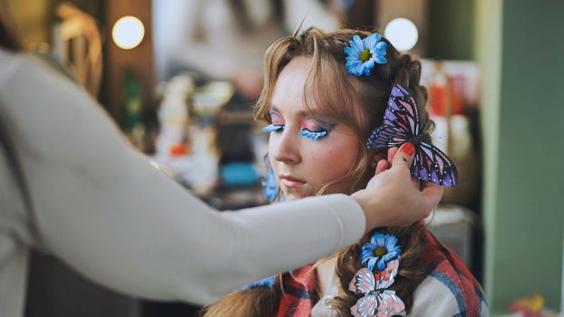 The hairdresser decorates the model's hair with blue flowers and butterflies.