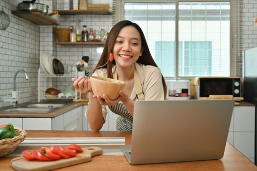 Portrait of attractive woman eating fresh salad in kitchen. Wellbeing and healthy lifestyle concept.