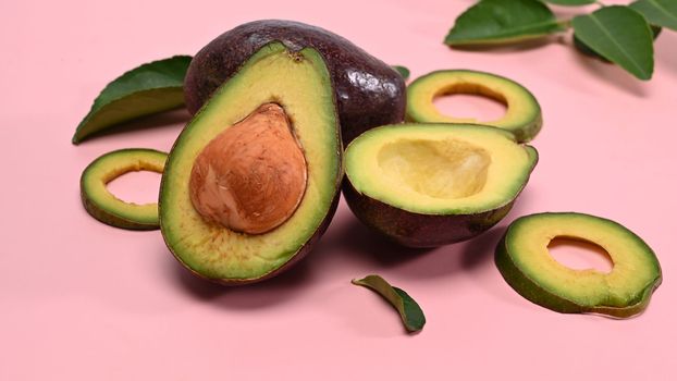 Fresh half and sliced avocado on pink background.