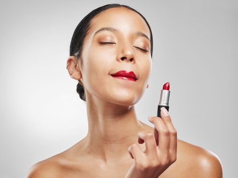 Theres a shade of red for every woman. Studio shot of a young woman applying red lipstick against a grey background.