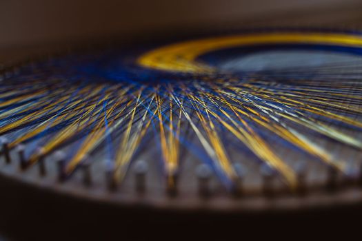 Colored thread mandala on a wooden board with nails. Mandala Moon Harmony Sun esotericism and psychology pictures from yellow and blue silk threads.