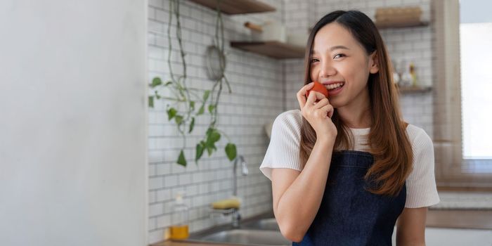 Portrait of Asian young woman look at camera. Attractive beautiful woman wear apron in cozy kitchen with fresh organic vegetables on table cooking healthy vegetable salad, healthy food active life