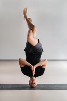 A man performs a yoga pose with support on his head in the gym. Yogi in a headstand