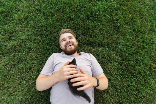 Man with little kitten lying and playing on grass - friendship love animals and pet owner concept
