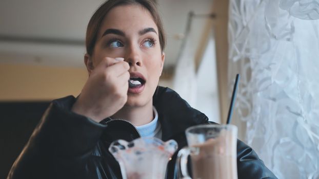 A girl is eating ice cream in front of a cappuccino in a coffee shop.