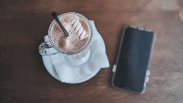 A girl drinking a cappuccino in front of her smartphone.