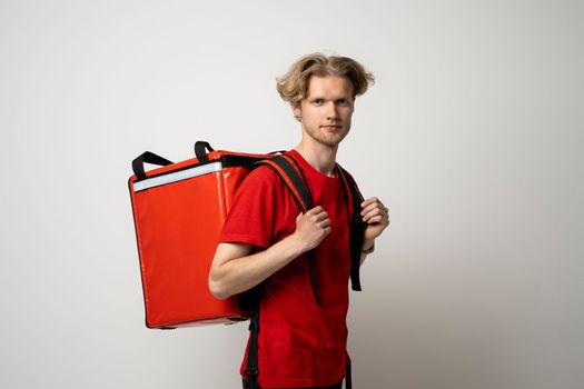 Young courier delivery man in red uniform with thermo bag isolated on white background. Delivery service.