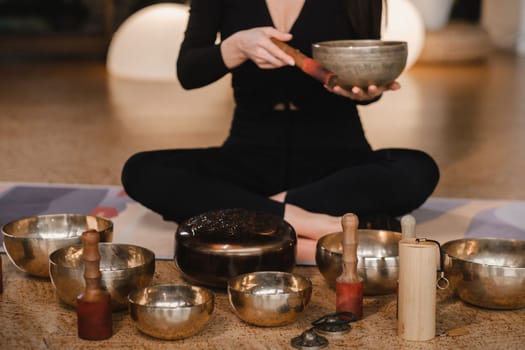 A woman in the lotus position using a singing bowl indoors . Relaxation and meditation. Sound therapy, alternative medicine. Buddhist healing practices