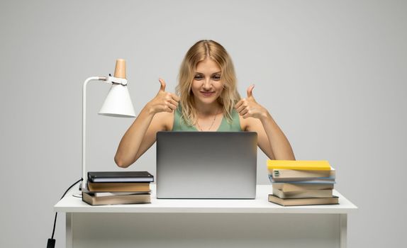 Cheerful office worker business student woman freelancer showing two thumbs up in front of laptop while speaking with a partners or clients.