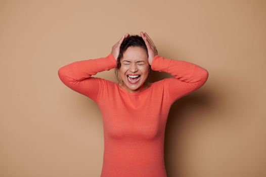 Beautiful multi-ethnic woman with her eyes closed screaming, isolated on beige color background