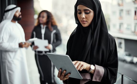 Shes at the top of her game. an attractive young businesswoman dressed in Islamic traditional clothing using a tablet on her office balcony.