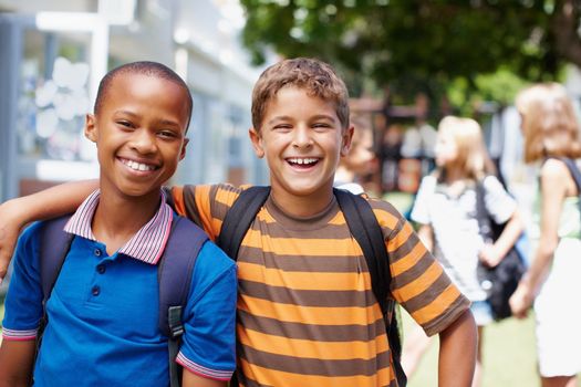 Encouraging great friendships in a positive environment. Two boys standing outside their school in casual clothes smiling happily at you - copyspace.