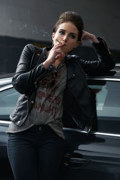 Attitude and attractive. a rebellious looking young woman smoking a cigarette in a car garage.
