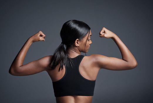 Great results only happen when great effort is put in. Studio shot of a young sportswoman flexing her biceps with her back turned to the camera against a gray background.