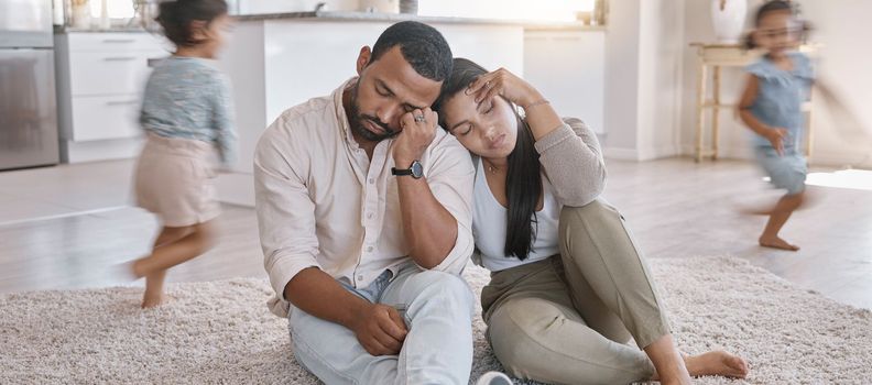 A young mixed race couple looking stressed at home while their kids play around them, Hispanic mother and father lacking energy as their kids play in the lounge at home