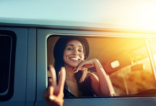 Happy road tripping. a young woman leaning out of a vans window and showing a peace sign on a roadtrip.