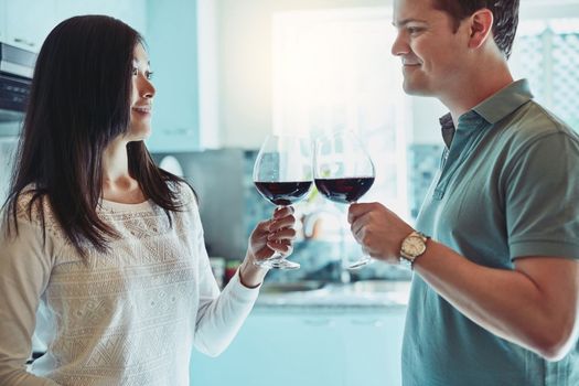 Heres to the best love story. a young couple enjoying a glass of wine at home.