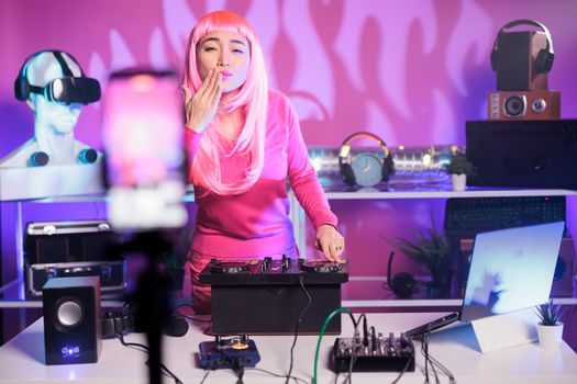 Artist with pink hair playing techno song at professional turntables while recording music process