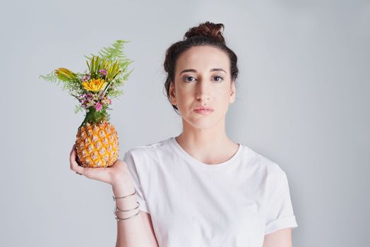 I like to decorate my fruit with flowers before I eat it. Studio shot of a beautiful young woman holding a pineapple against a grey background.