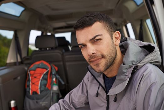 Just gotta get my gear together. Portrait of a handsome young hiker sitting at the bank of a car before his hike.