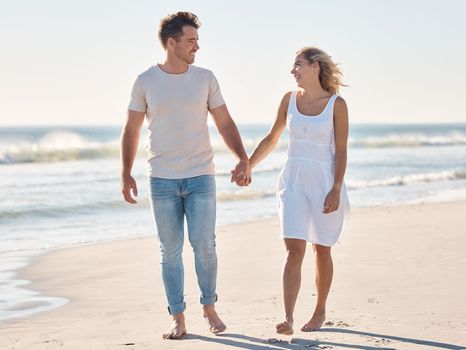 Couple, holding hands and walking on the beach for love, care or relationship bonding together in the outdoors. Happy man and woman relaxing on a lovely walk on the sandy ocean coast for romance.
