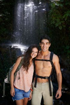 No vacation is complete without some adventure. Portrait of a beautiful young couple standing in a shady spot near a waterfall.