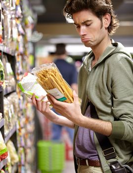 Whats the difference. A young man with two products in his hands in a grocery store.