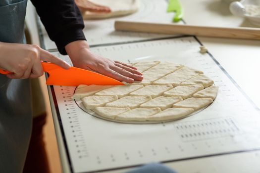 Side view of cutting dough with a plastic knife on a silicone baking mat
