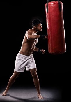 I dont need a weapon...I am one. Studio shot of kick boxer working out with a punching bag against a black background.
