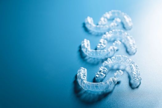 background for dental clinic or orthodontics. invisible plastic new braces lie in a row on a blue background, studio shot with shadows