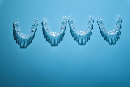 background for dental clinic or orthodontics. invisible plastic new braces lie in a row on a blue background, studio shot with shadows