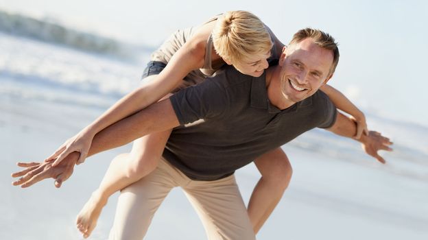 Laughter is the secret to a great relationship. A husband giving his wife a piggyback ride on the beach.