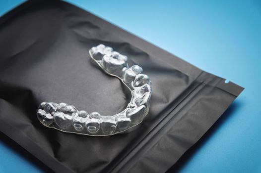 close-up, invisible plastic braces on a black special zip package, lying on a blue background. studio shot, dental clinic background.